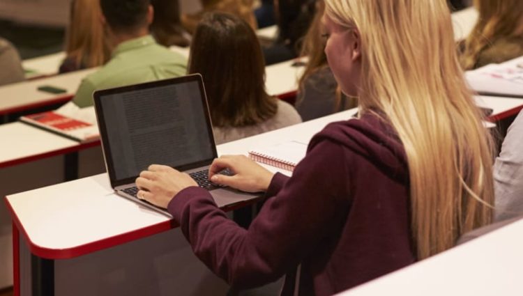 Photo of woman typing on laptop in lecture hall.