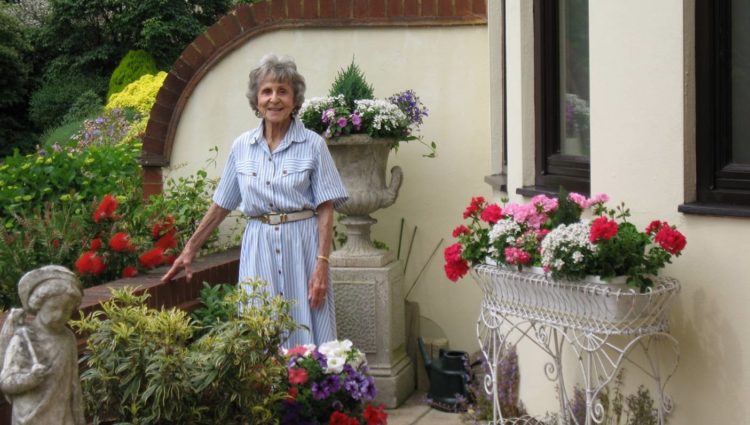 Patricia Powell stood in a garden with bots of brightly coloured flowers around her.