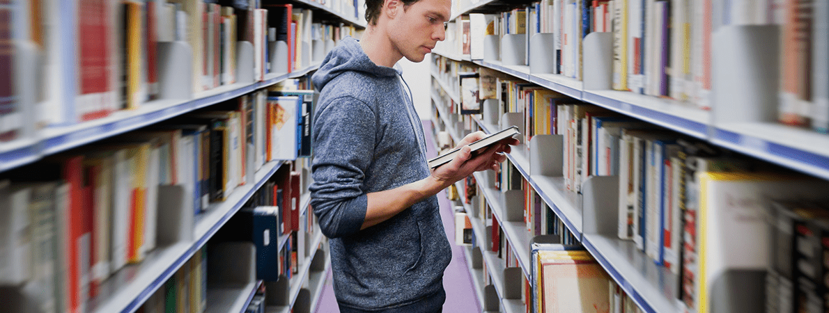 Male student standing in library reading a book