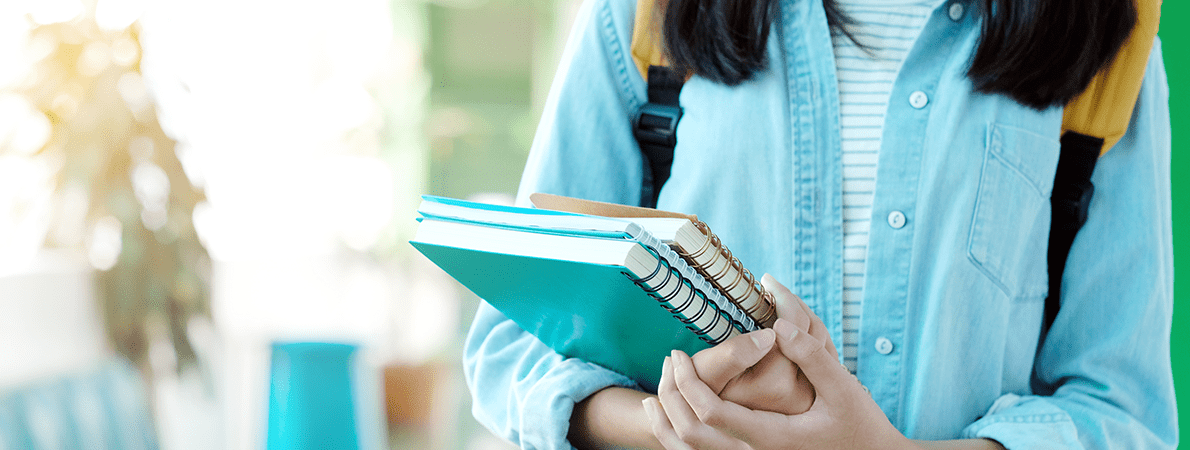 Close up of female student holding a stack of notepads waking down a university corridor