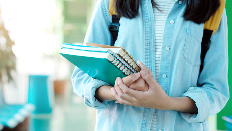 Close up of female student holding a stack of notepads waking down a university corridor