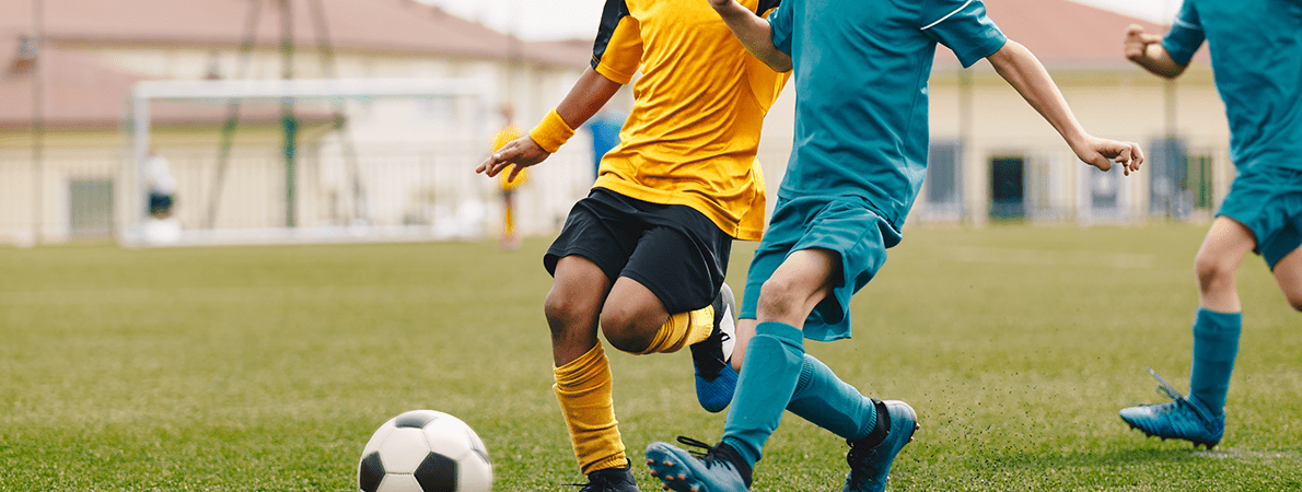 Close up of boys playing football. One is in a yellow football strip, the other in blue
