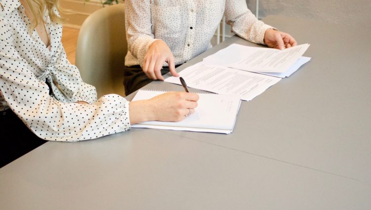 Two women sat at a desk writing on a stack of paper