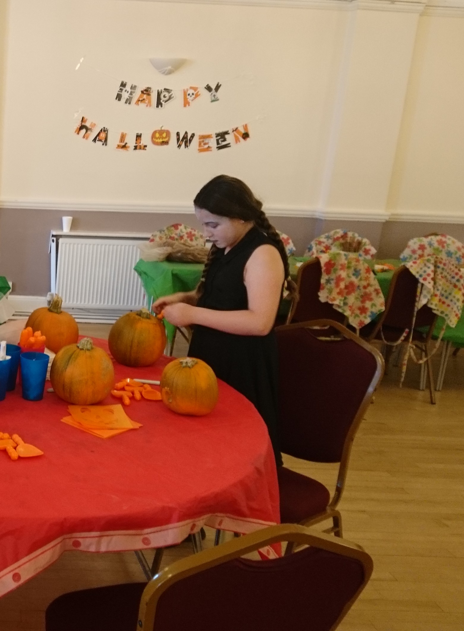 A young woman hand carving pumpkins sitting on a table. Background decoration saying 'Happy Halloween'