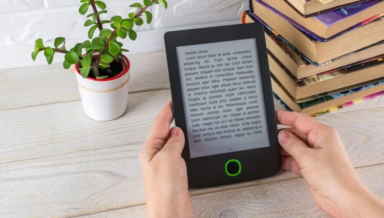 Person holding a tablet with a text, on a desk, with some books and a plant on it