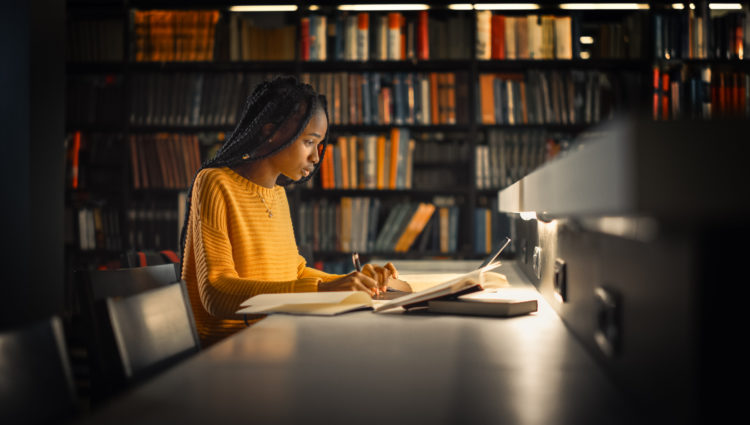 girl in a yellow jumper writing nots in a library