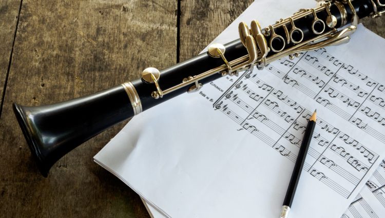 Close up picture of a clarinet on a wooden table, some music sheets and a pencil