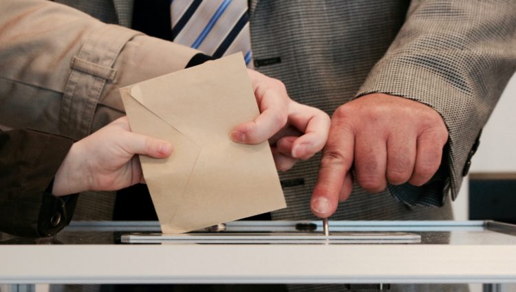 A ballot paper is being inserted into a ballot box.