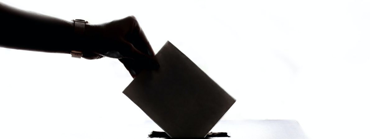 A voting slip is being inserted into a ballot box.