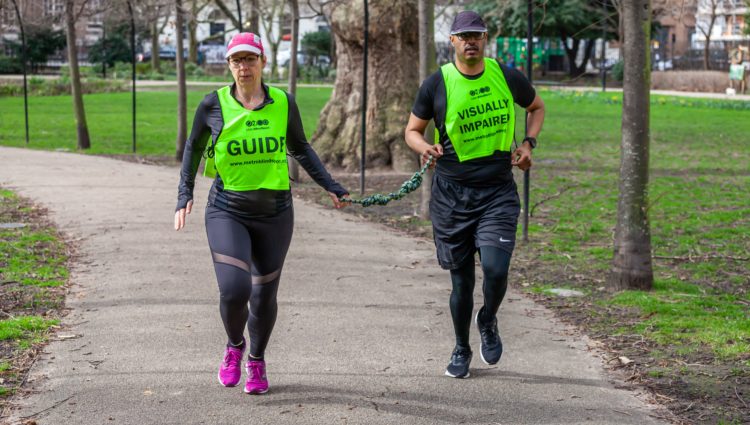 A visually impaired person running at the park guided by a woman