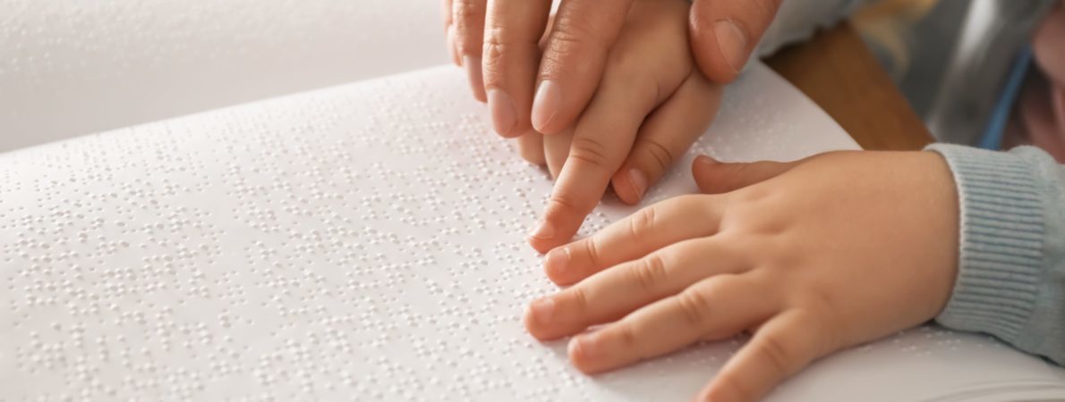 Close up picture of an adult helping a kid when reading braille