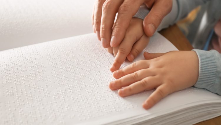 Close up picture of an adult helping a kid when reading braille