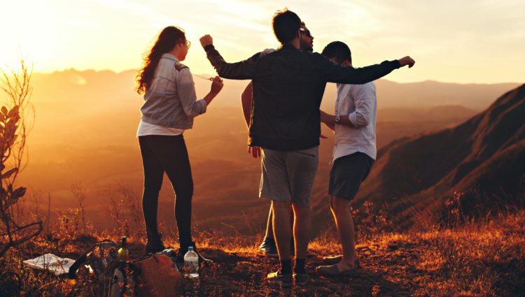 A group of four young people enjoying the sunset view on a hill